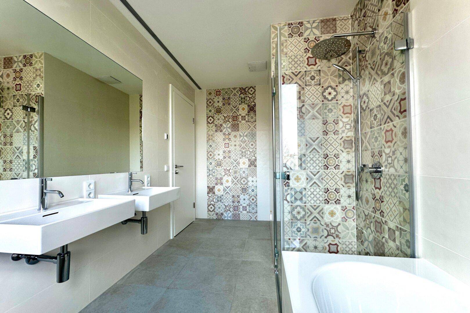 Modernes Badezimmer mit Doppelwaschbecken, Badewanne und Dusche, verziert mit gemusterten Fliesen.