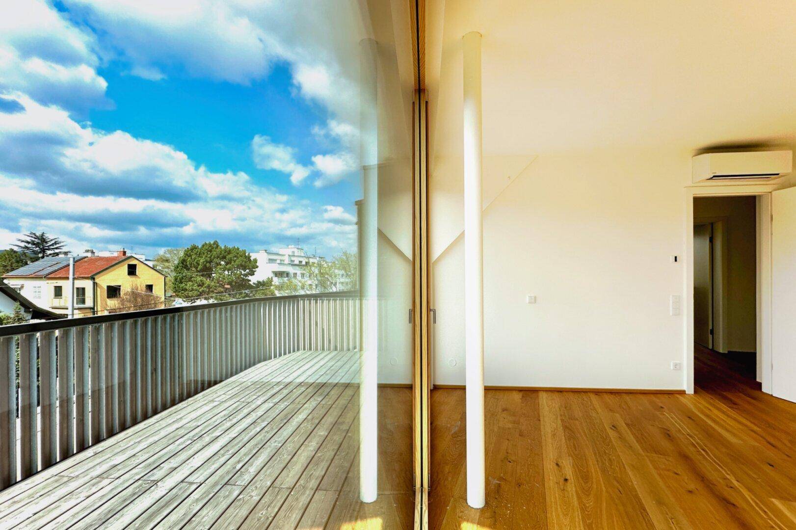 Lichtdurchfluteter Raum mit Holzboden und Zugang zum Balkon, ausgestattet mit Klimaanlage.