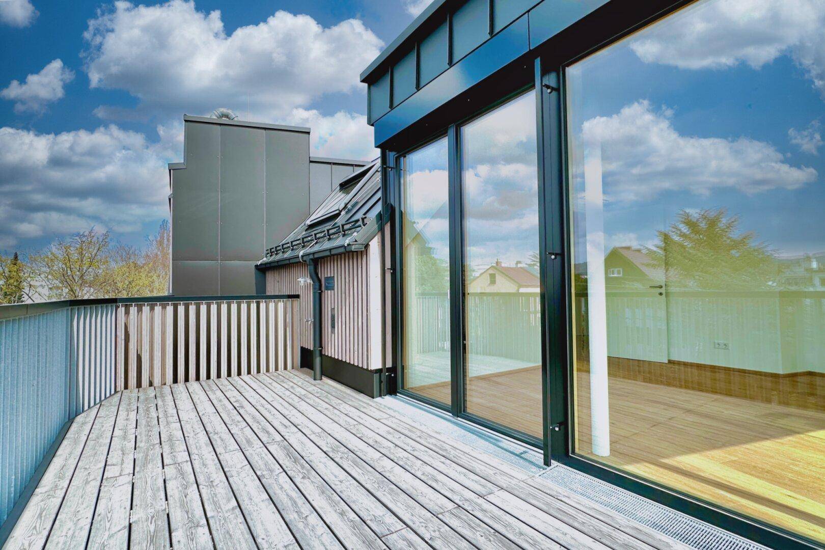 Moderner Balkon mit Holzboden und großen Glasfronten, die viel Licht in den Innenraum lassen.
