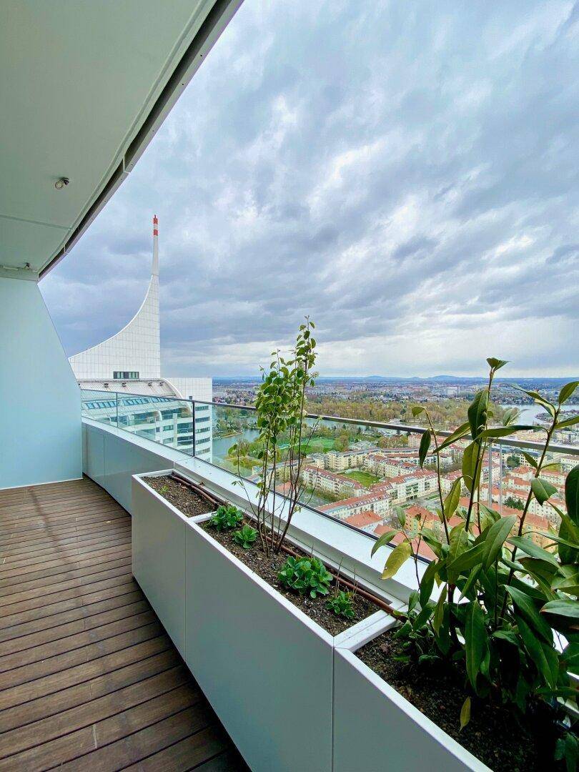 Balkon mit Holzboden und Pflanzenkübeln, bietet einen weiten Blick über die Stadt und die Umgebung.