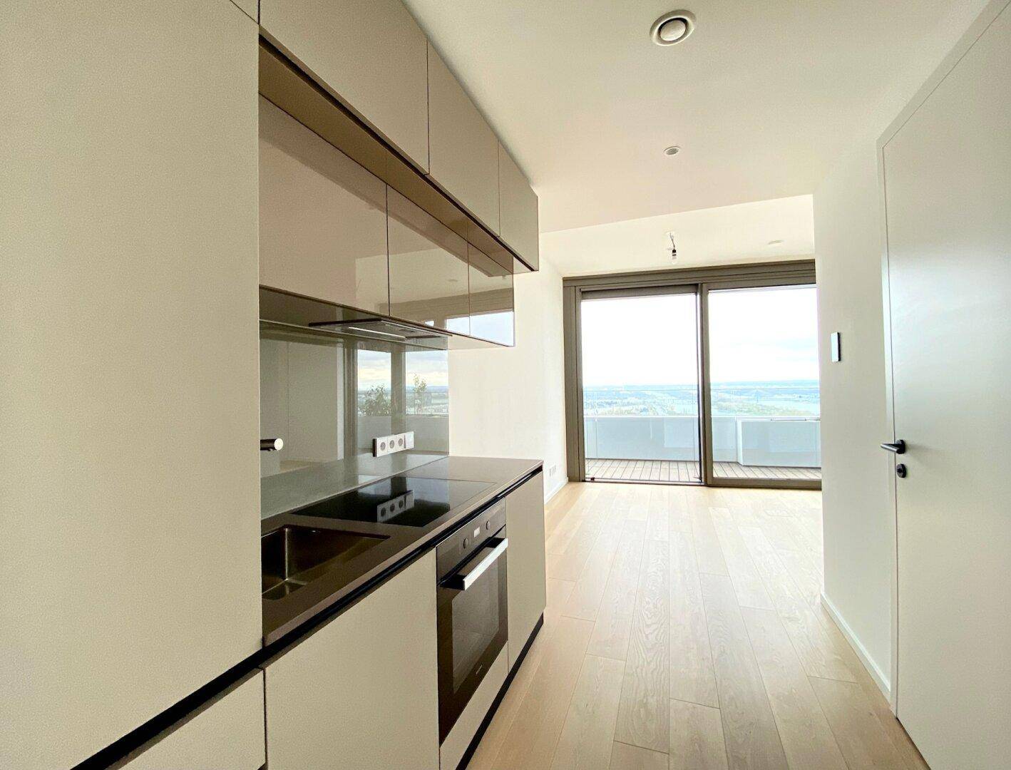 Offene Küchenzeile mit modernen Geräten und Blick auf den Balkon durch große Fenster.