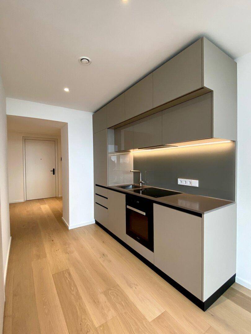 Moderne Einbauküche in neutralen Farbtönen mit integrierten Geräten und Holzboden.