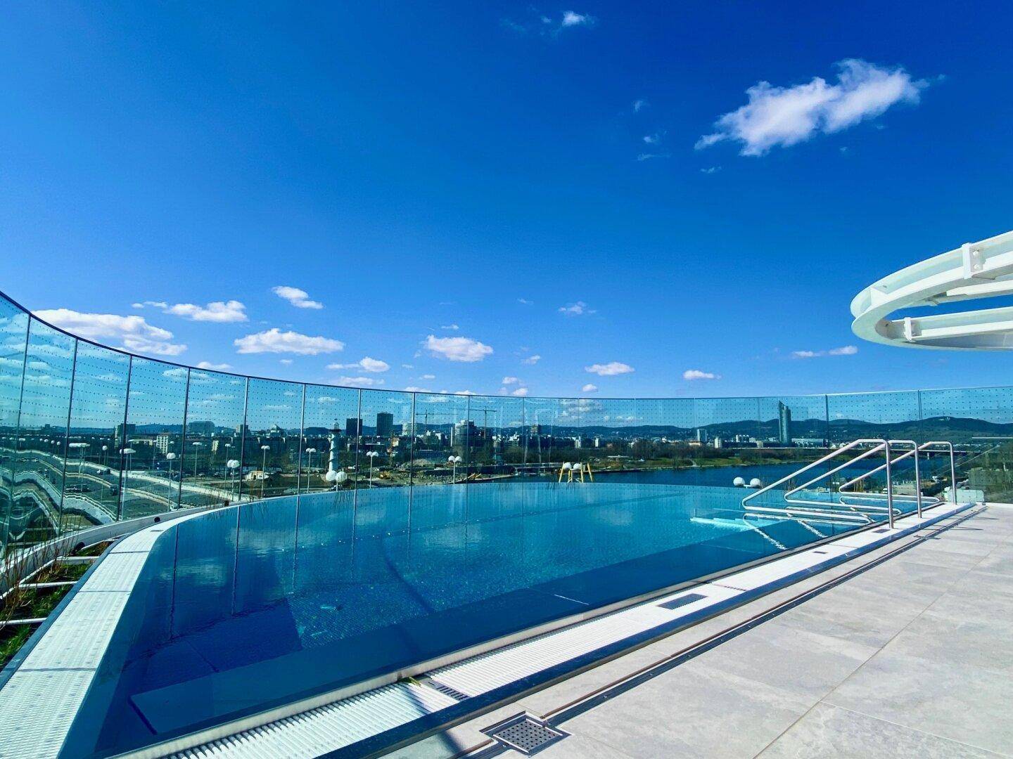 Infinity-Pool auf dem Dach mit Glasgeländer und Panoramablick auf die Stadt und den Fluss.
