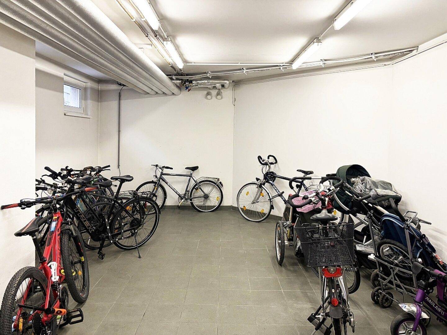Heller Fahrradraum mit vielen Fahrrädern und Kinderwagen.