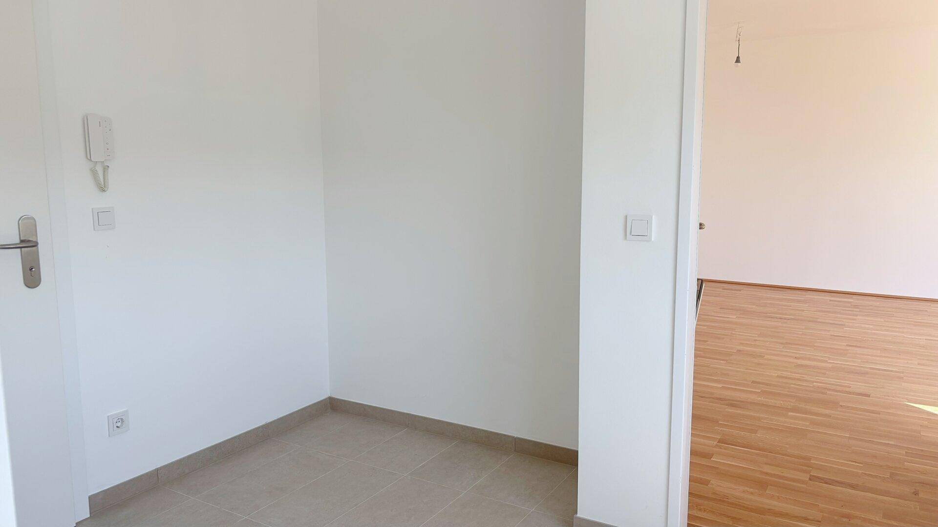 Eingangsbereich mit Fliesenboden und Gegensprechanlage, der zu weiteren Räumen führt.