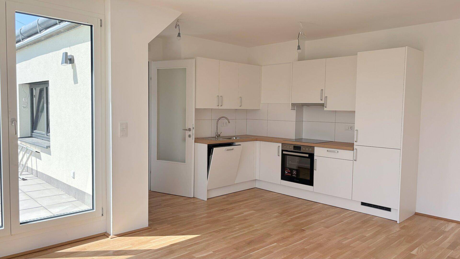 Moderne Einbauküche mit weißen Schränken, Holzarbeitsplatte und Zugang zur Terrasse.