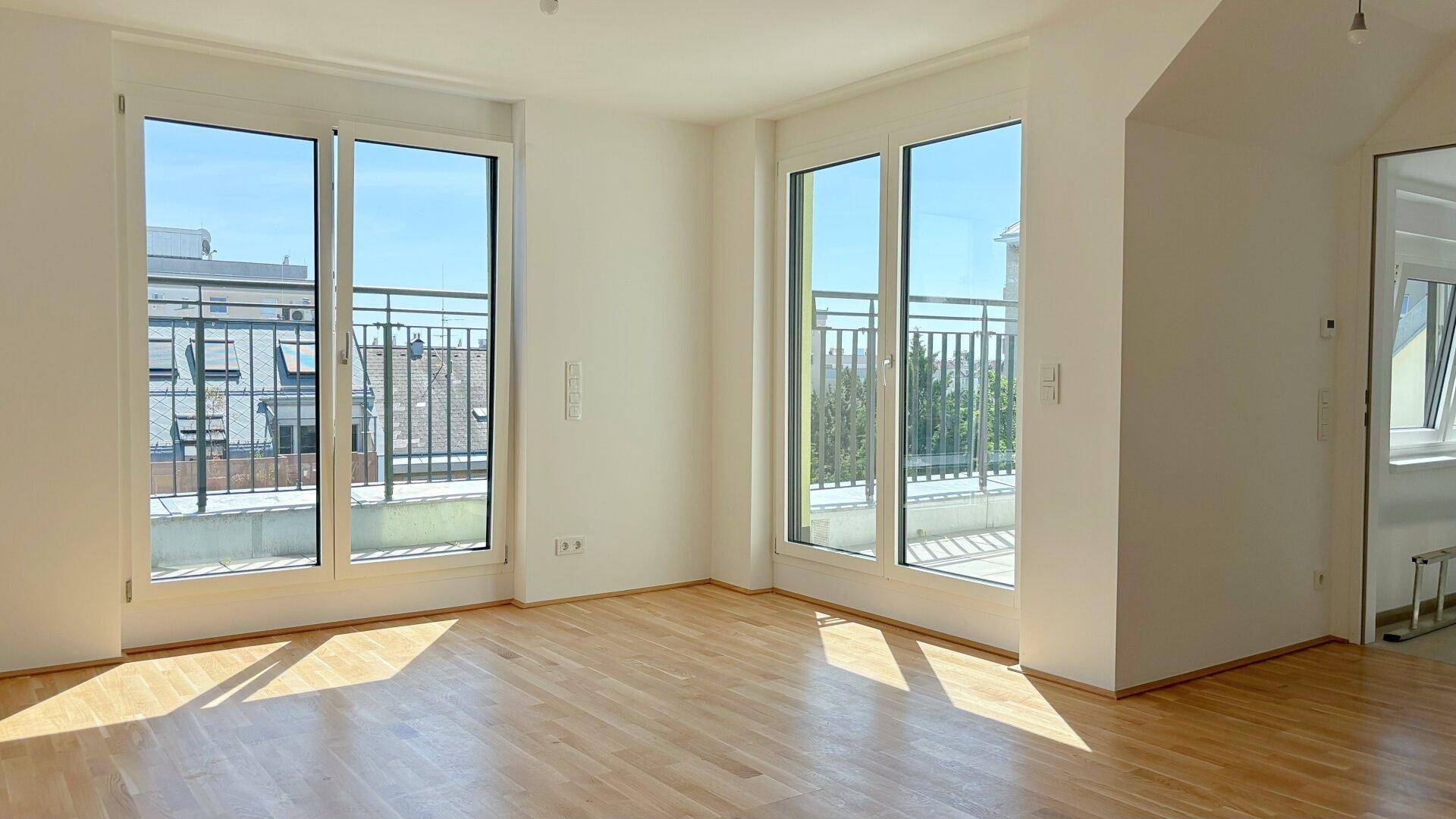Heller Wohnraum mit großen Fenstern, Holzboden und Zugang zu einem Balkon.