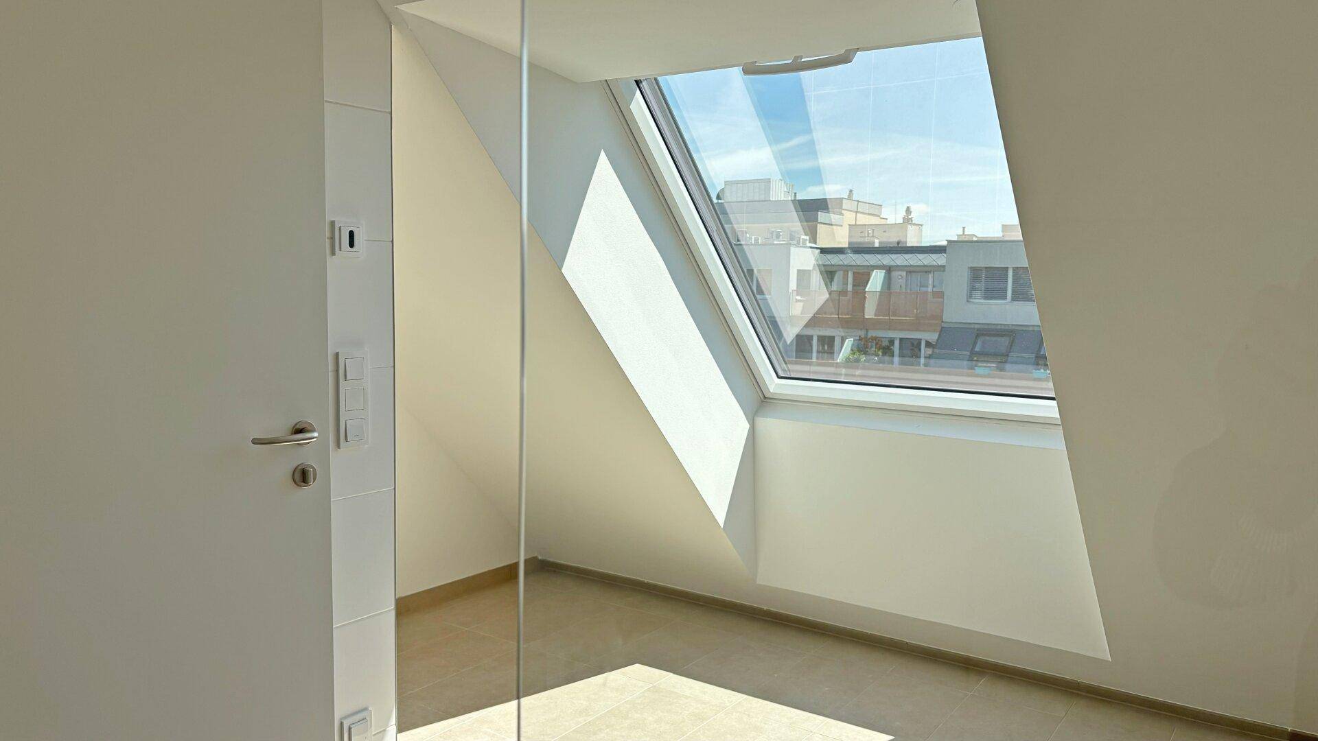 Heller Raum mit Dachfenster, schräger Decke und moderner Glastrennwand.