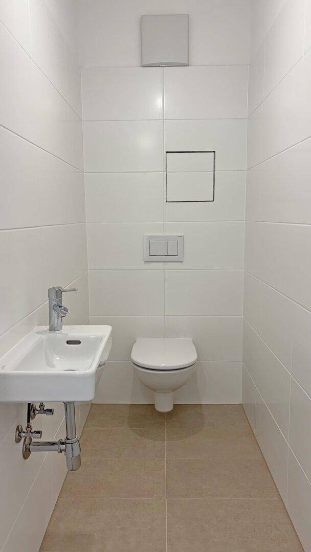 Separates Gäste-WC mit Wand-WC, kleinem Waschbecken und hellen Fliesen.