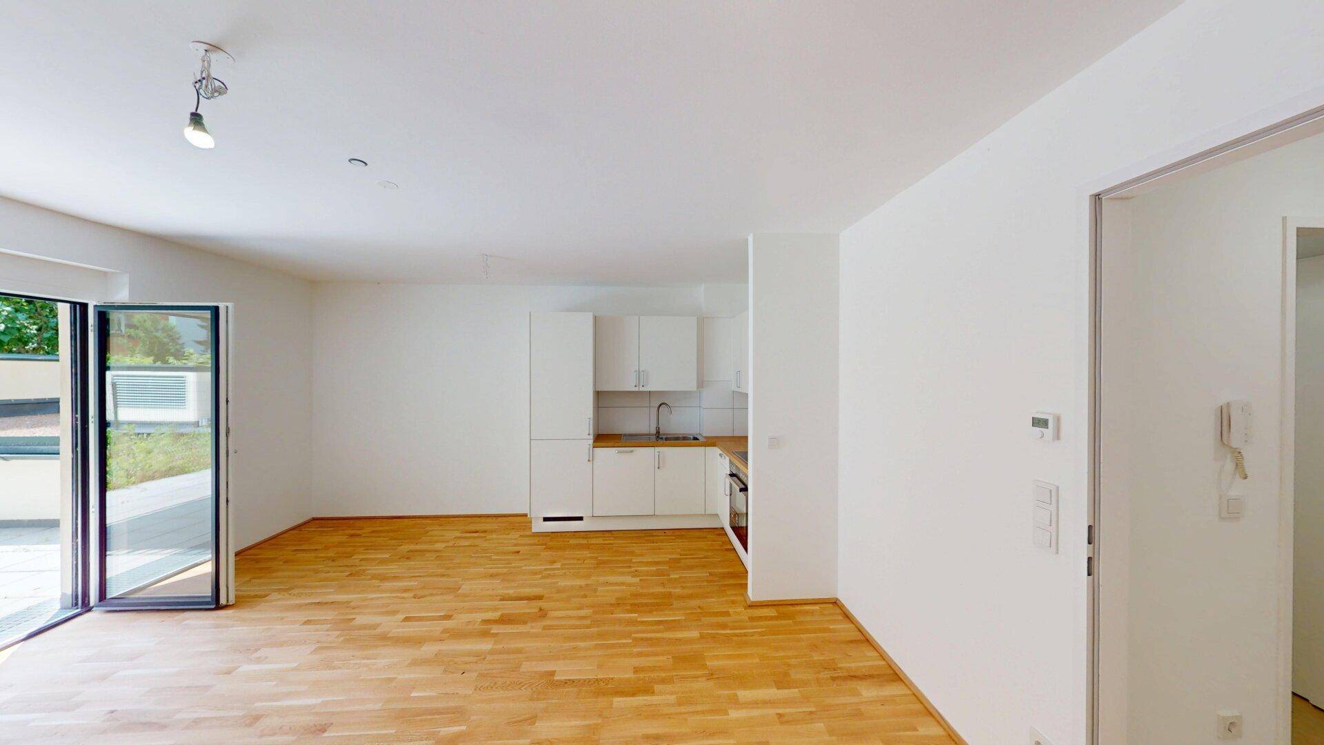 Geräumiger, heller Wohnbereich mit Parkettboden und einer funktionalen, weißen Küchenzeile.
