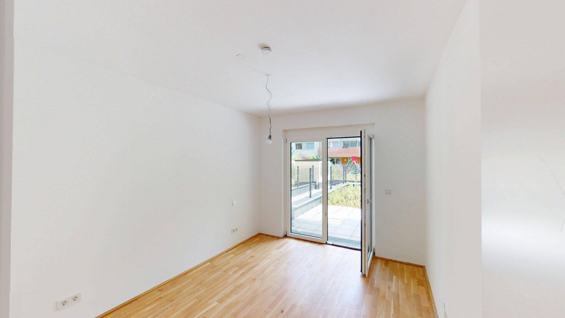 Helles Zimmer mit Parkettboden und Zugang zu einem kleinen Außenbereich, ideal als Schlafzimmer.