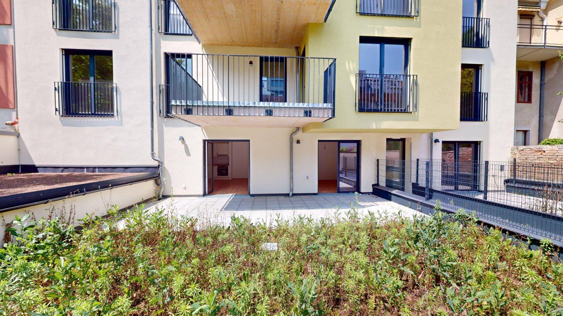 Ansicht der modernen Wohnanlage mit mehreren Balkonen und einer weitläufigen Terrasse im Erdgeschoss.