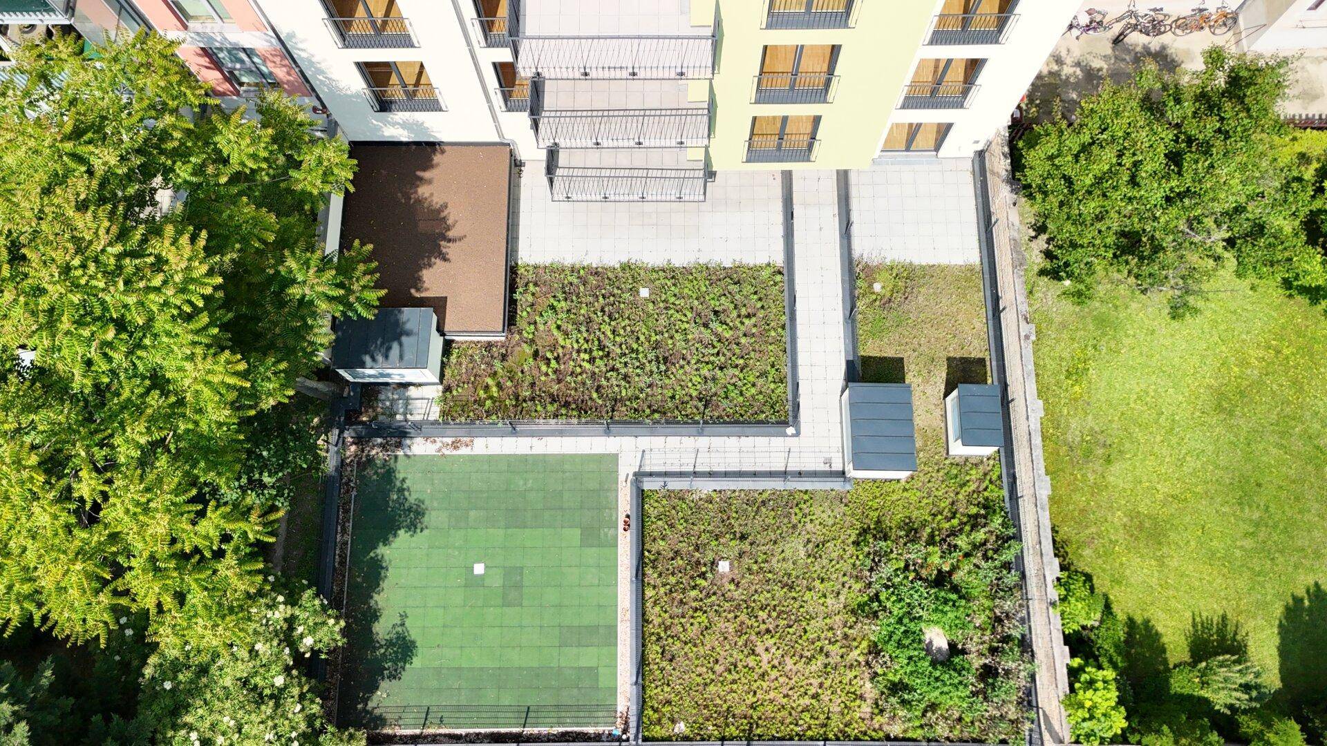 Luftaufnahme des begrünten Innenhofs mit verschiedenen Gartenbereichen und einer gepflasterten Terrasse.