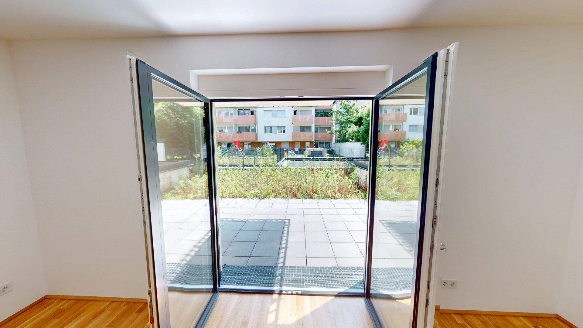 Große Fensterfront im Wohnbereich mit Blick auf die Außenterrasse und die umliegenden Gebäude.