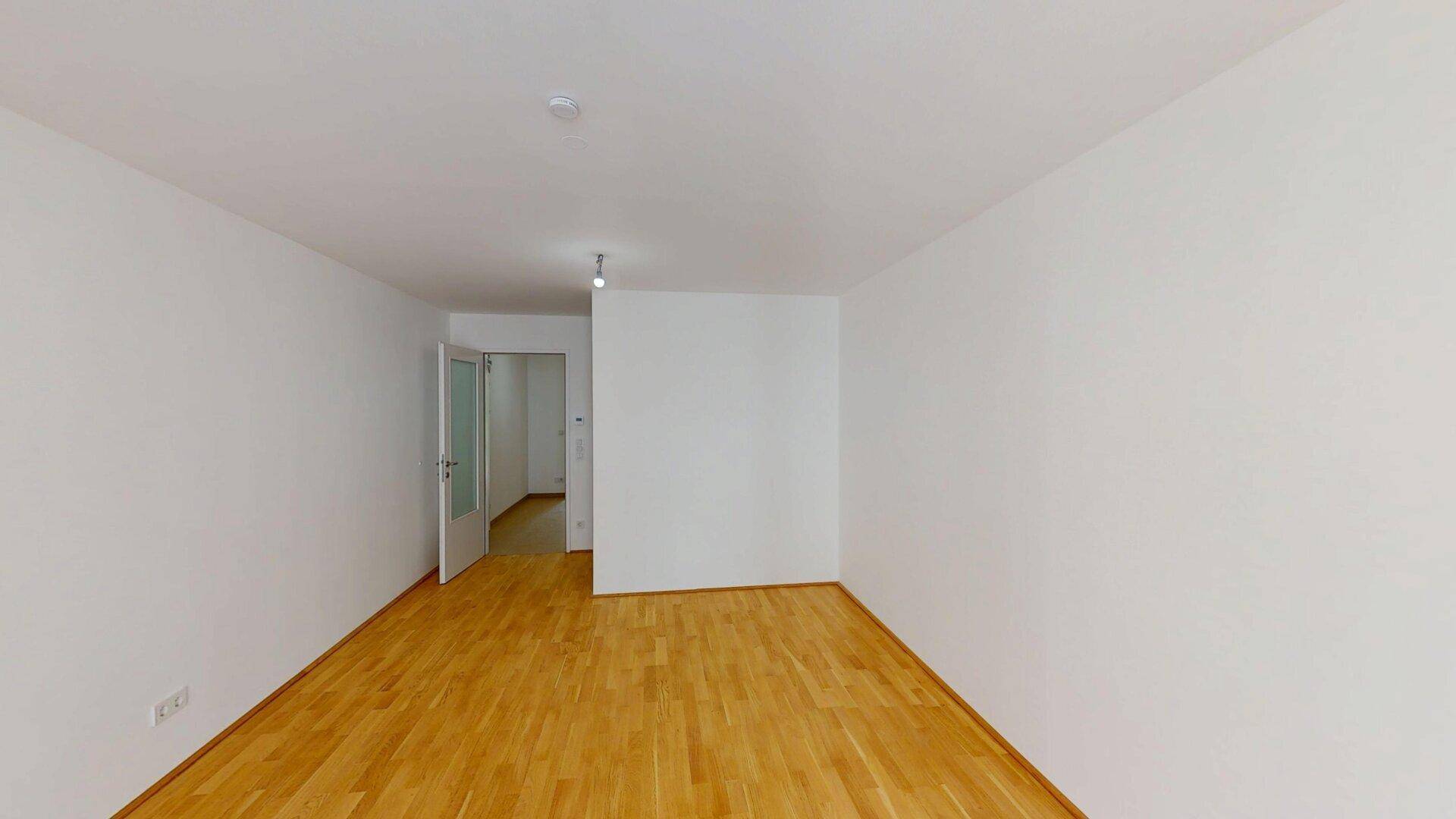 Leeres Zimmer mit Parkettboden und Zugang zu weiteren Räumen, ideal für individuelle Gestaltung.