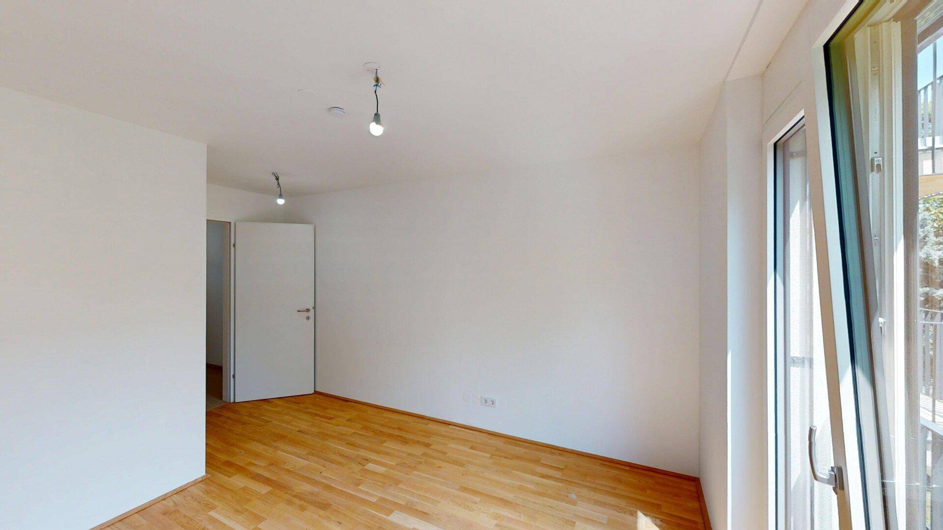 Heller Wohnraum mit Parkettboden und Zugang zu einem Balkon, bereit zum Einzug.