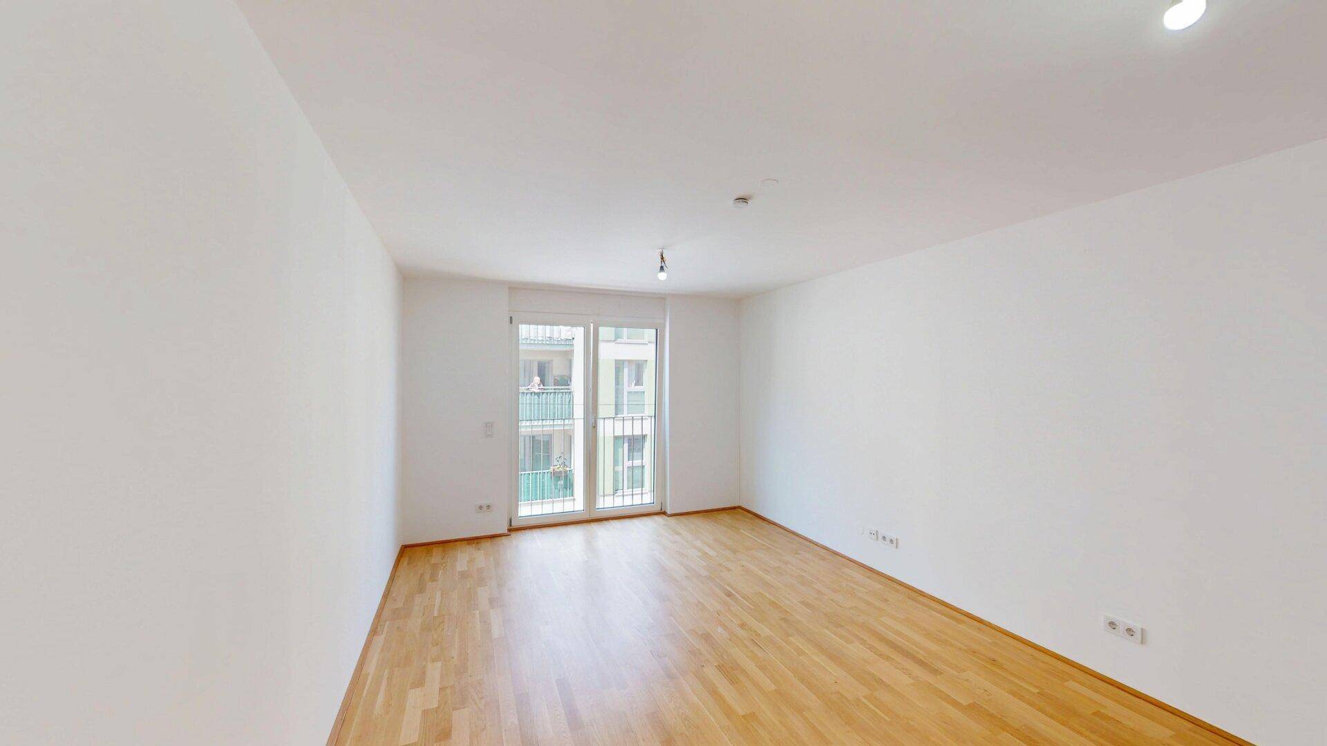 Helles, leeres Zimmer mit Parkettboden und Zugang zu einem französischen Balkon.