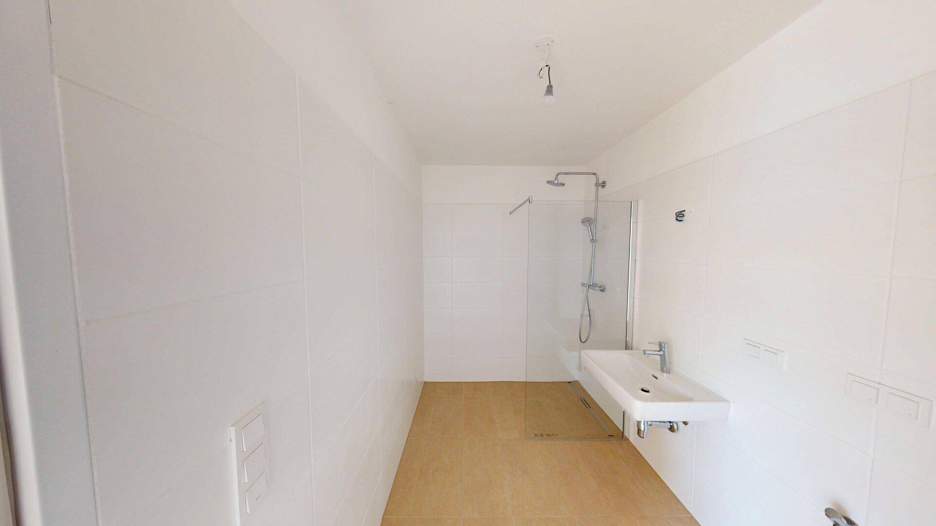 Modernes Badezimmer mit ebenerdiger Dusche, weißem Waschbecken und hellen Fliesen.