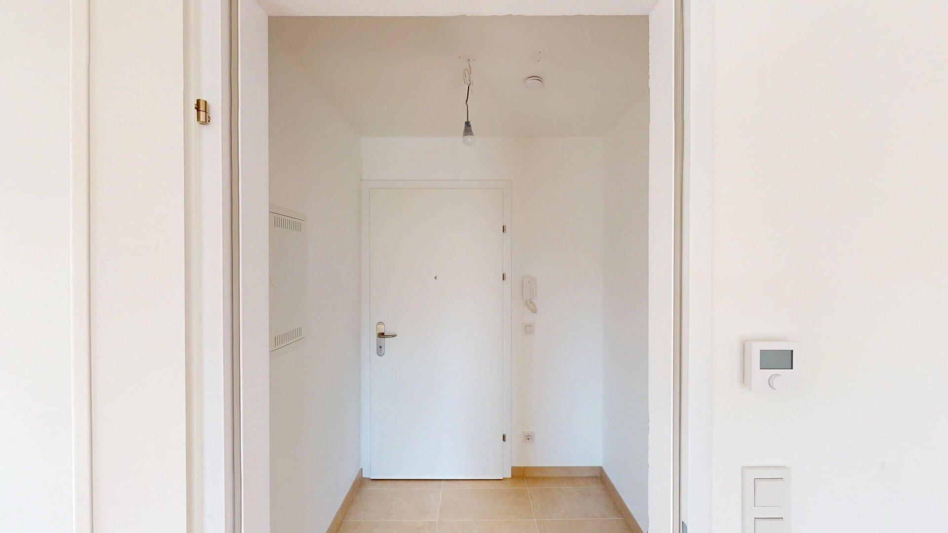 Heller Eingangsbereich mit Fliesenboden und Gegensprechanlage, führt zur Wohnungstür.
