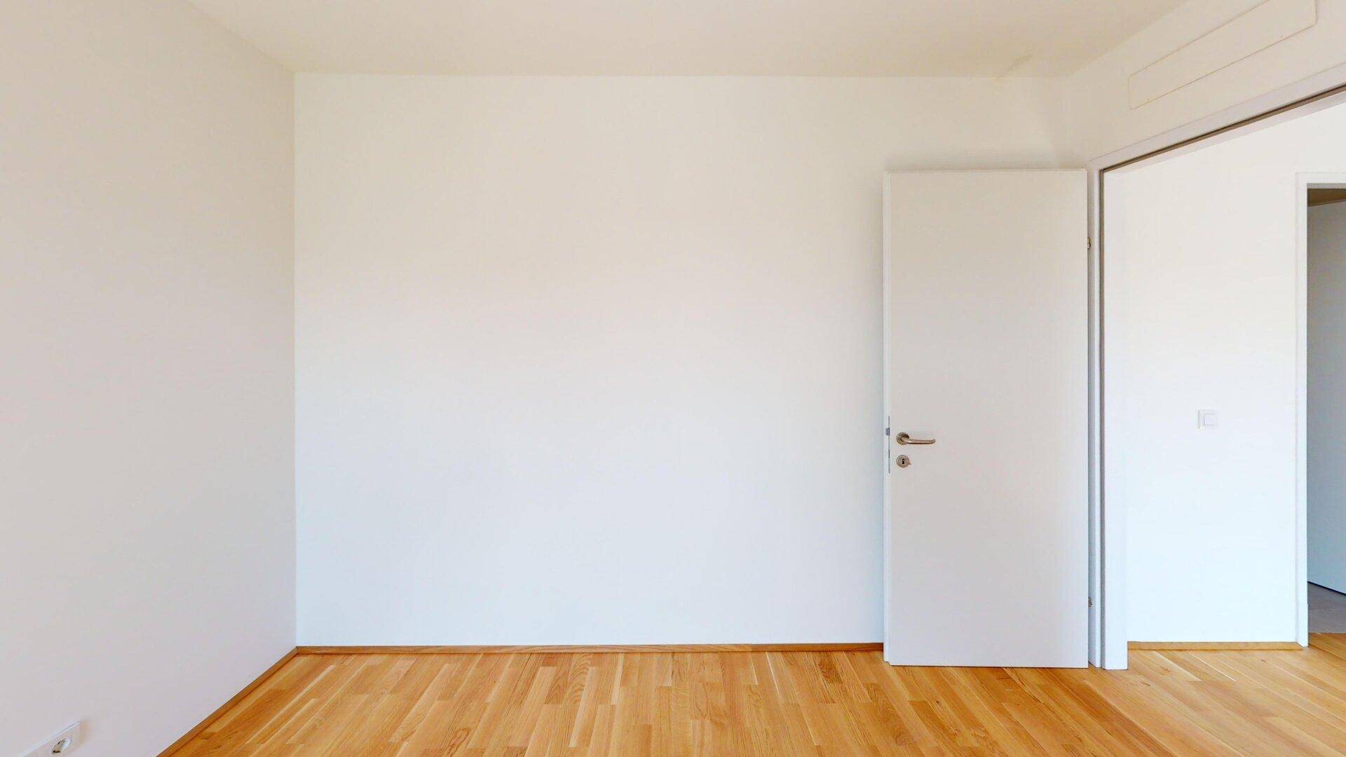 Leeres Zimmer mit hellem Parkettboden und weiß gestrichenen Wänden, bereit zum Einzug.