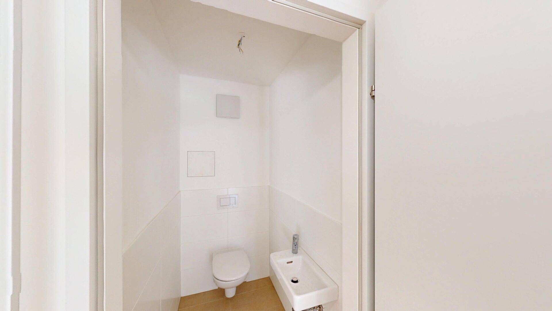 Kleines Gäste-WC mit wandhängender Toilette und Handwaschbecken, hell gefliest.