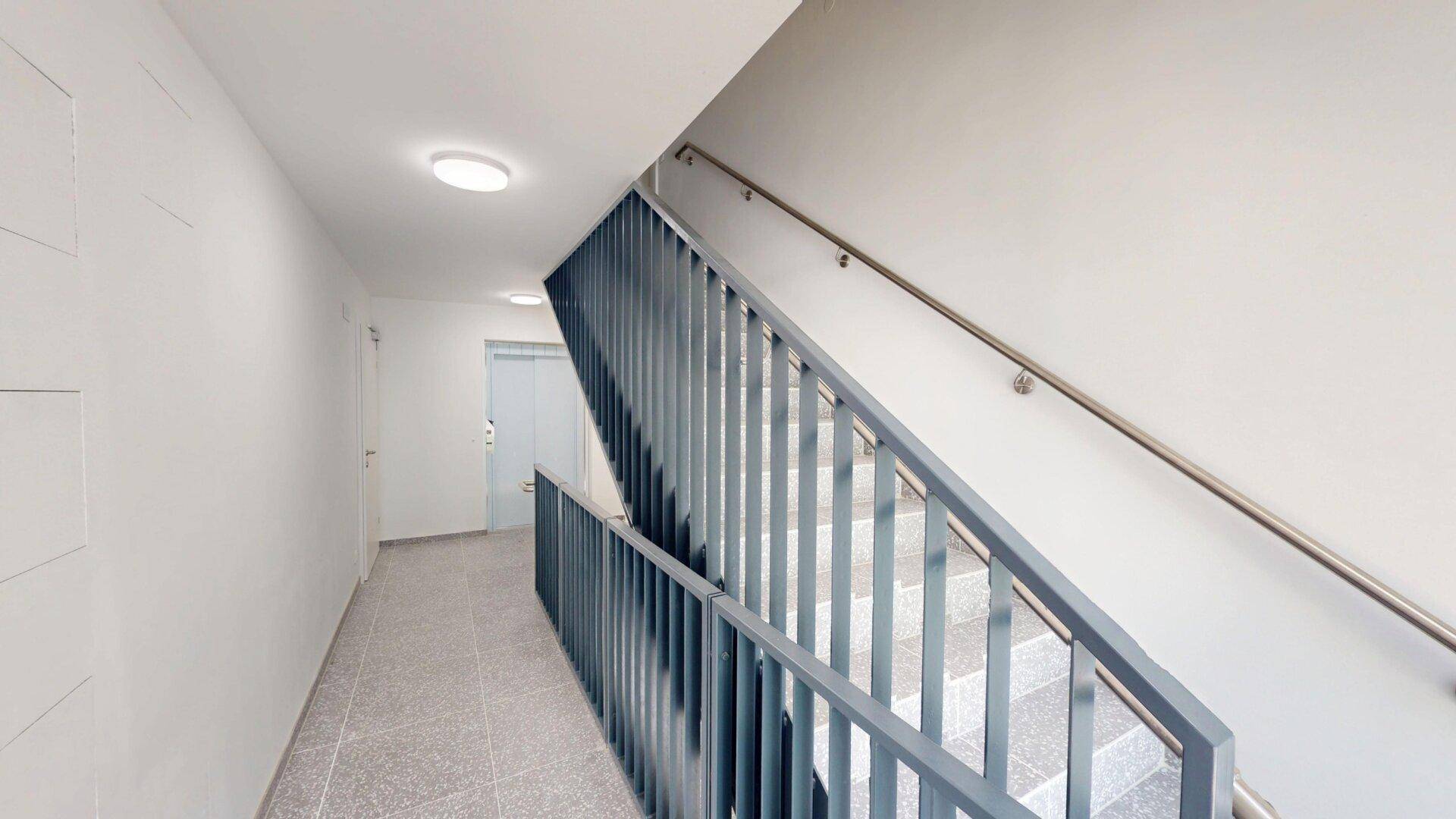 Heller Treppenaufgang mit modernem Geländer und Fliesenboden im Mehrfamilienhaus.