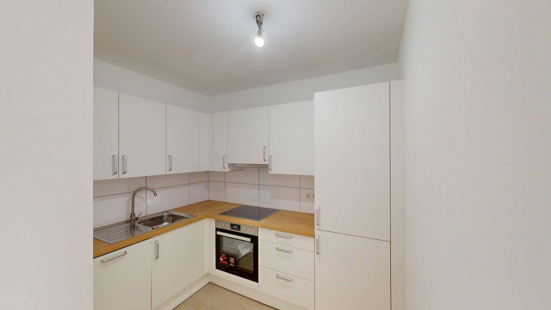 Moderne Einbauküche mit weißen Schränken, Holz-Arbeitsplatte und integrierten Geräten.