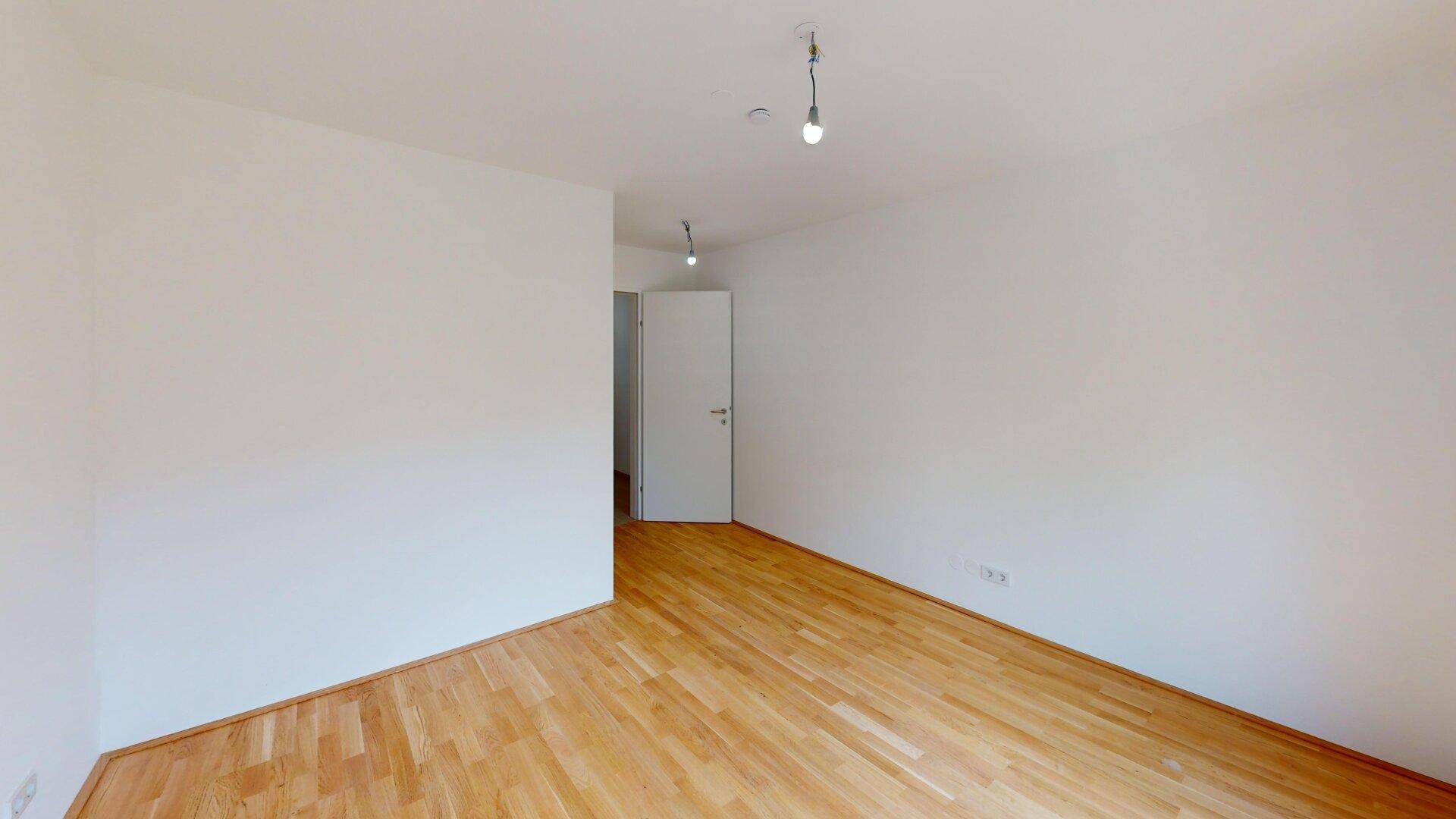 Leeres Zimmer mit hellem Parkettboden und weiß gestrichenen Wänden, ideal für individuelle Einrichtung.