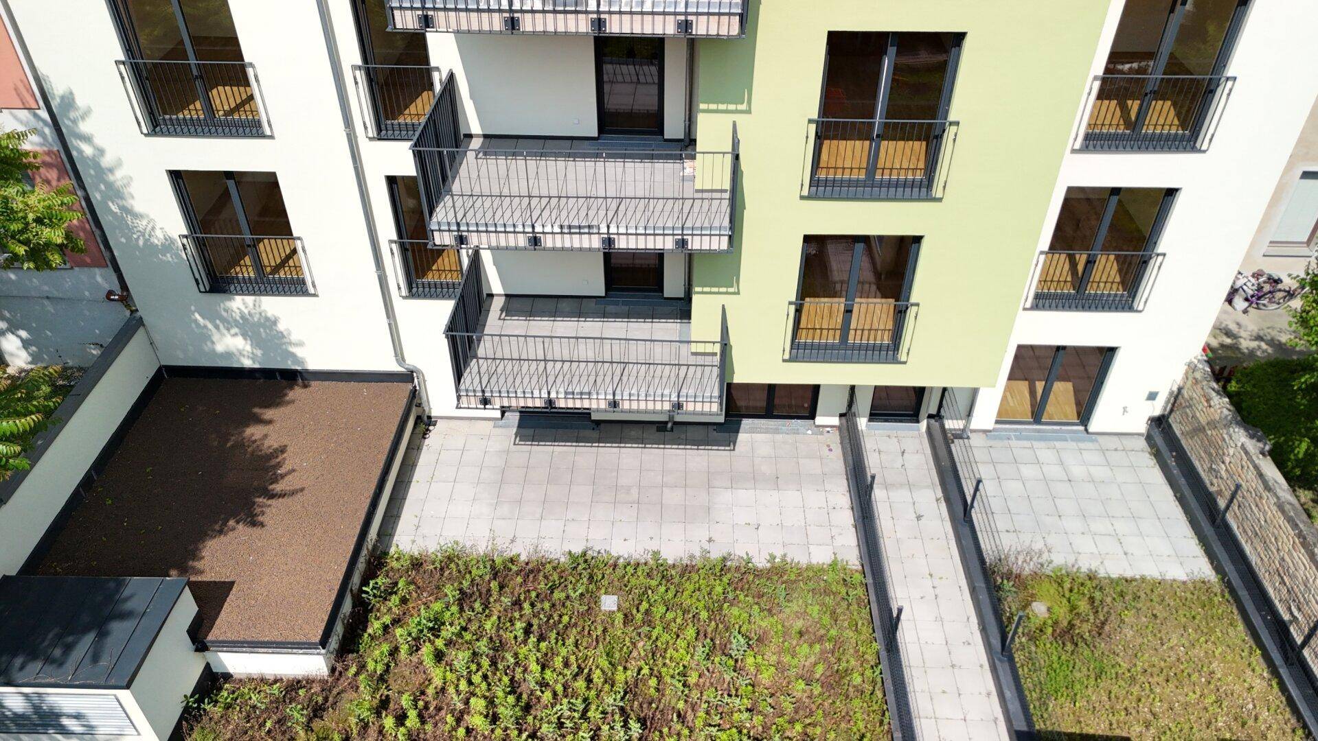 Begrünte Außenanlage mit gepflasterten Wegen und Terrassenbereichen am modernen Wohngebäude.