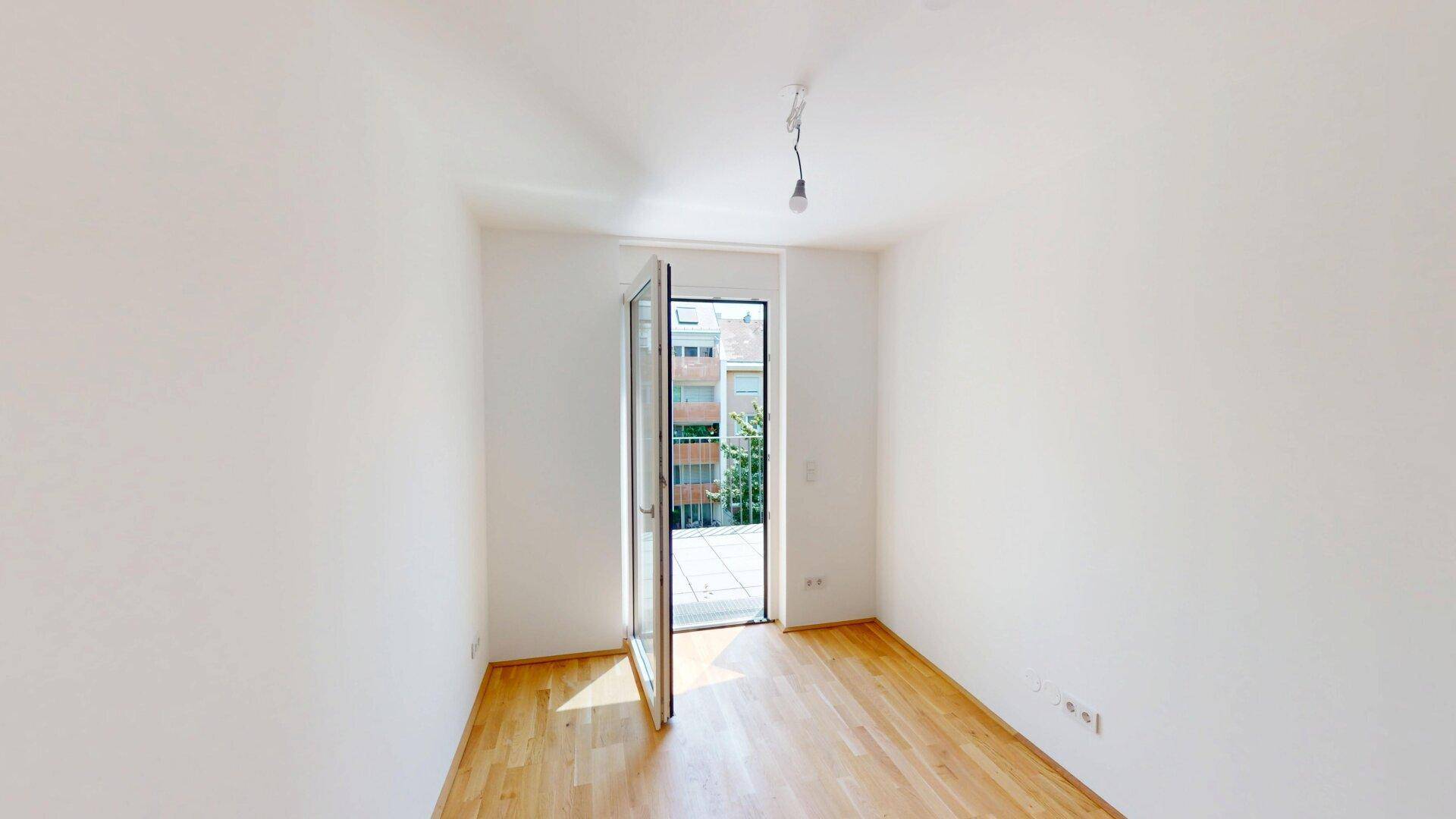 Lichtdurchflutetes Zimmer mit Parkettboden und Zugang zu einem kleinen Balkon, bereit zum Einrichten.