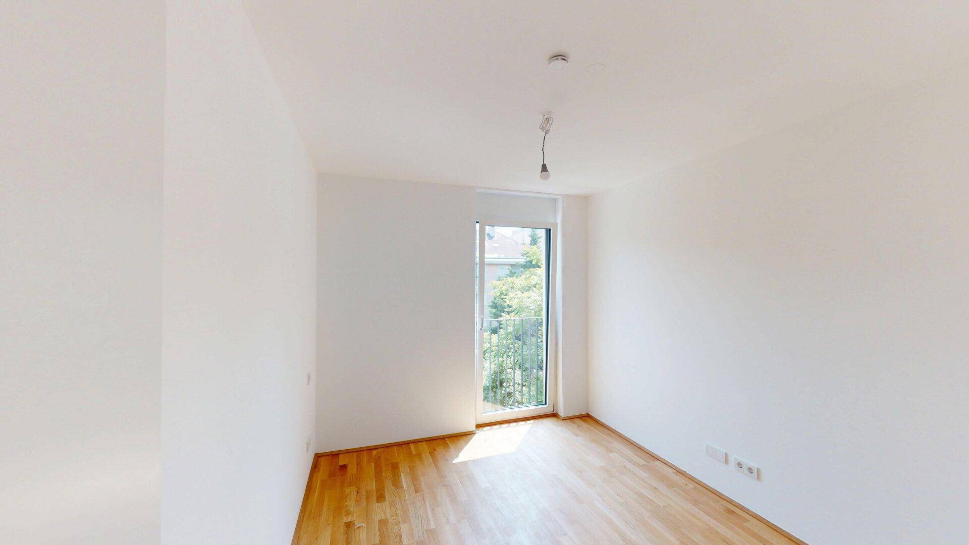 Geräumiges Zimmer mit Parkettboden und Fenster, das viel natürliches Licht bietet.