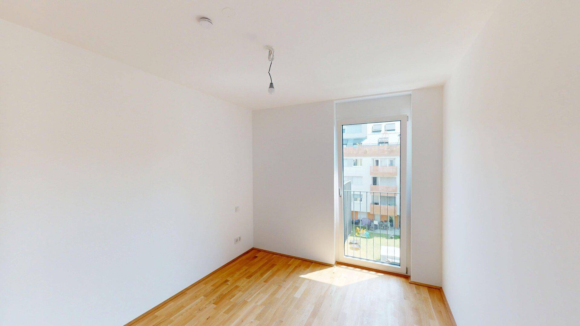 Helles Zimmer mit Parkettboden und großem Fenster, das viel Tageslicht hereinlässt.