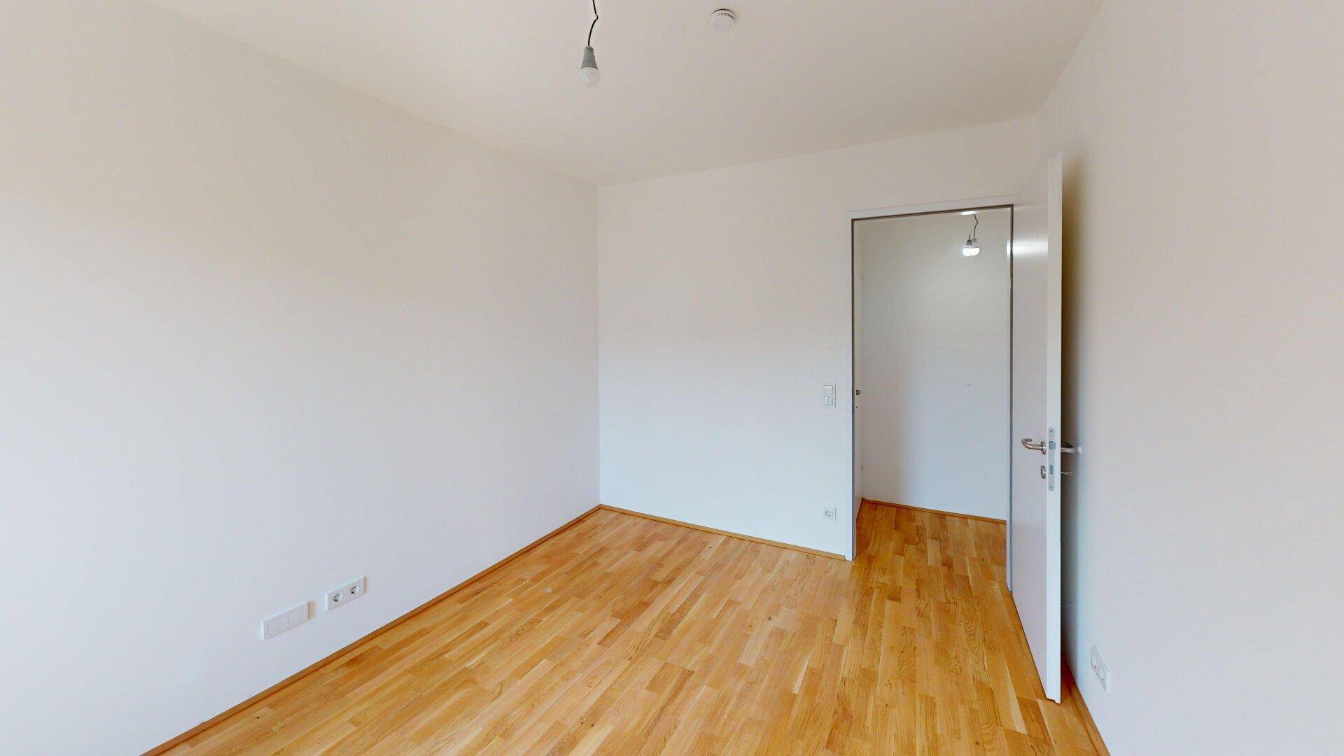Leeres Zimmer mit hellem Parkettboden und weiß gestrichenen Wänden, ideal für ein Schlafzimmer.