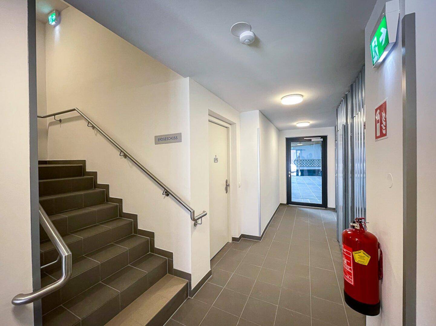 Heller Eingangsbereich mit Treppe, Handlauf und Zugang zum Gebäude.