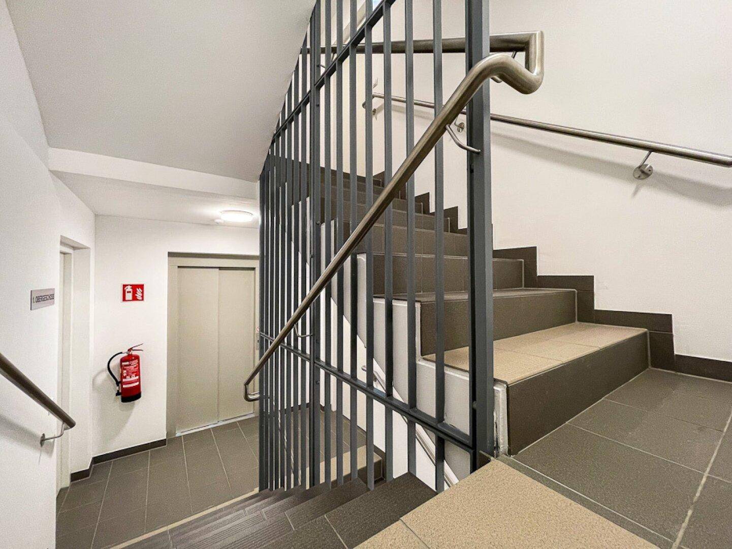 Modernes Treppenhaus mit Metallgeländer und Aufzug in einem Mehrfamilienhaus.