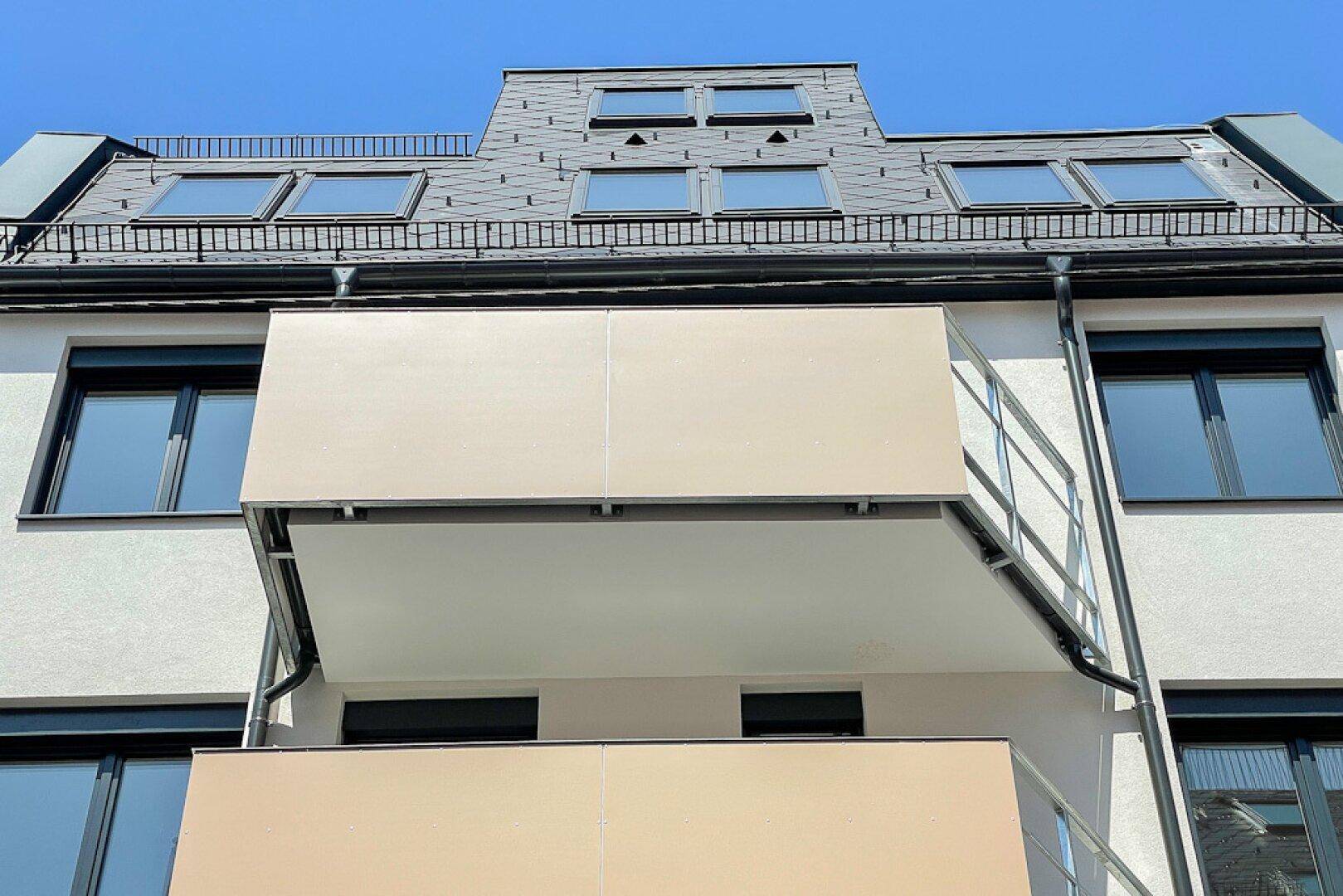 Moderne Gebäudefassade mit Balkonen und Dachfenstern unter blauem Himmel.
