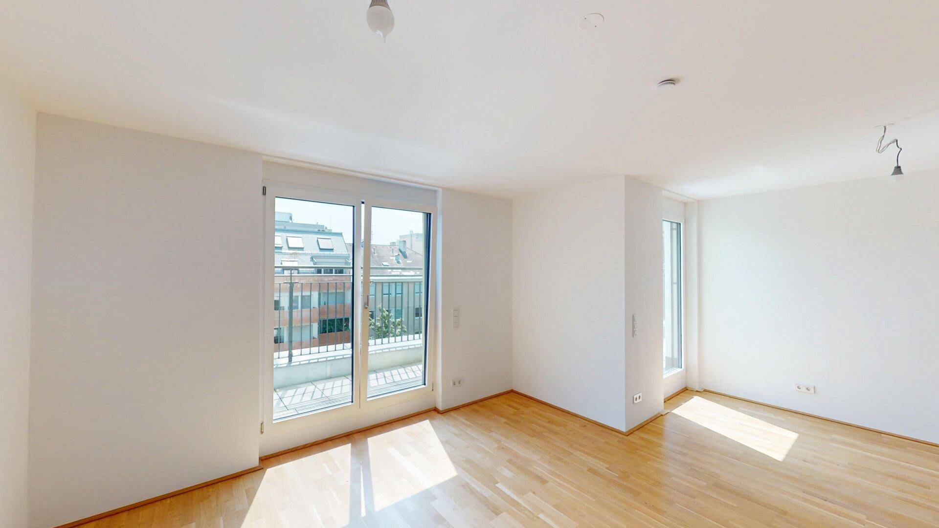 Lichtdurchfluteter Wohnraum mit Holzboden und Zugang zu einem Balkon.