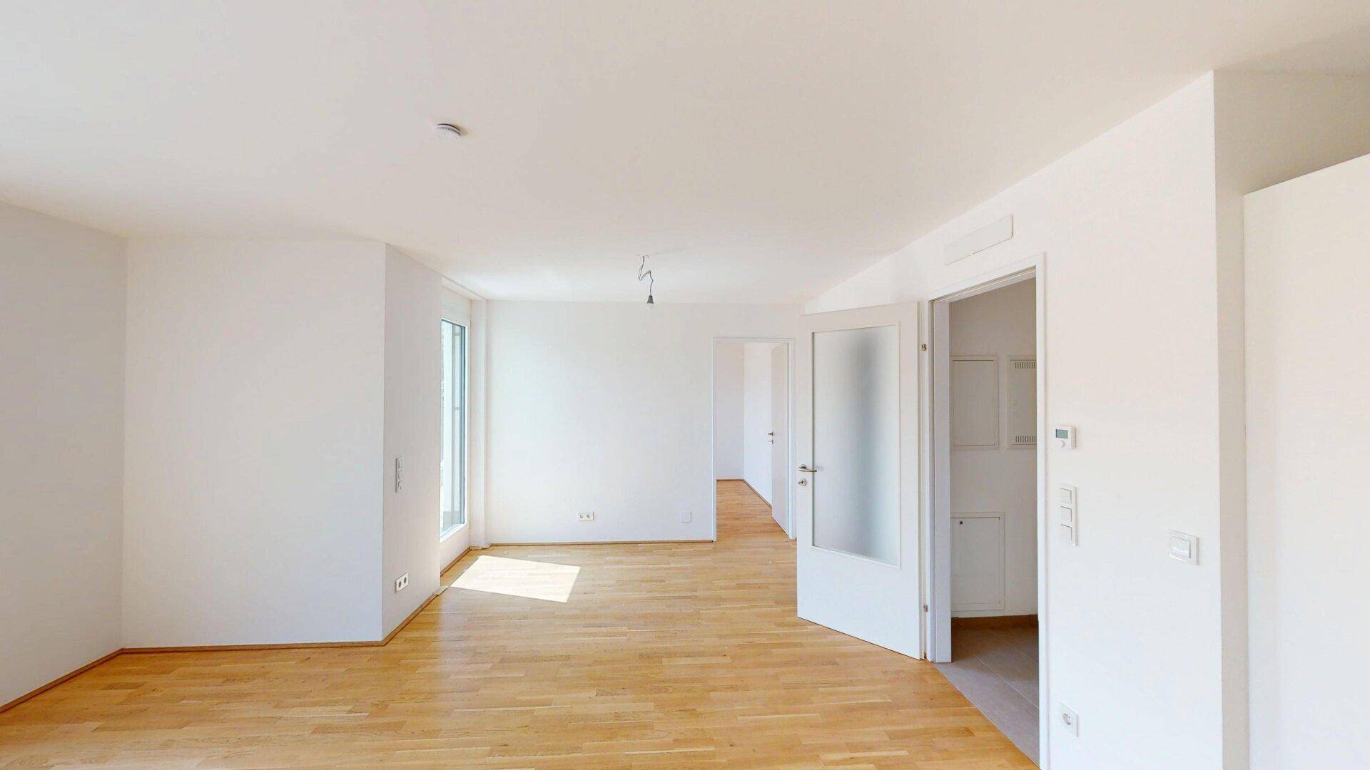 Heller Wohnraum mit Parkettboden und Zugang zu weiteren Zimmern durch Glastüren.