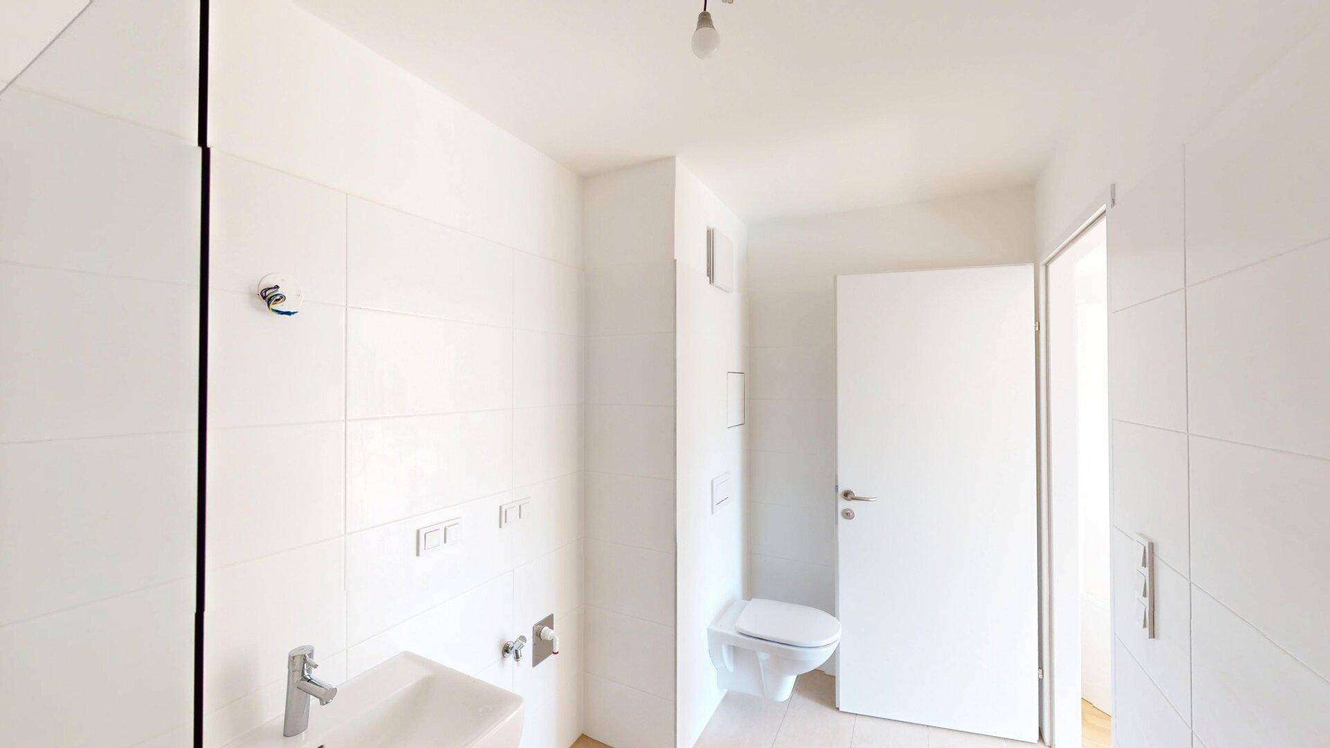 Helles WC mit wandhängender Toilette und kleinem Waschbecken, komplett gefliest.