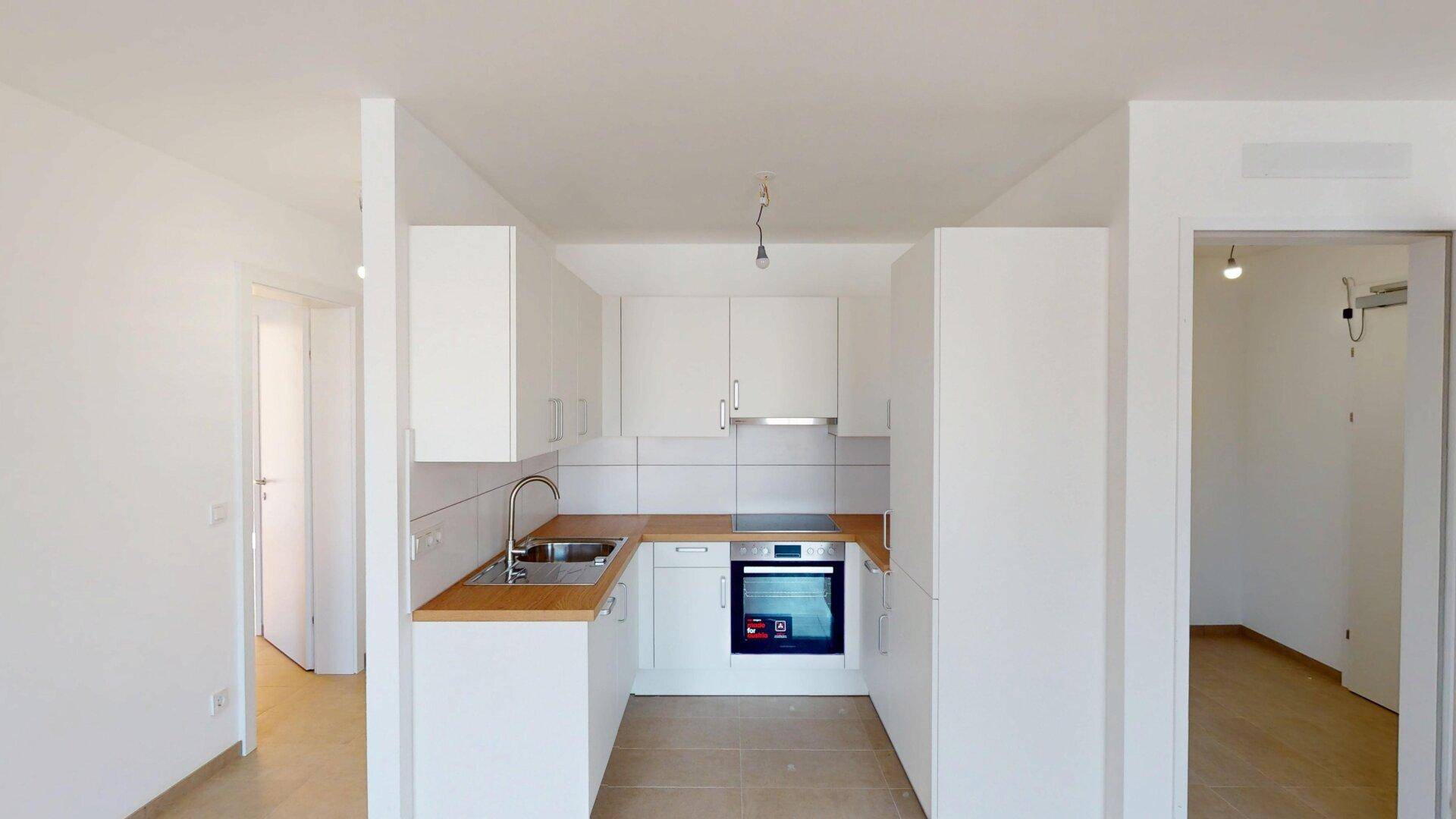 Moderne Einbauküche mit weißen Schränken, Holzarbeitsplatte und integriertem Backofen.