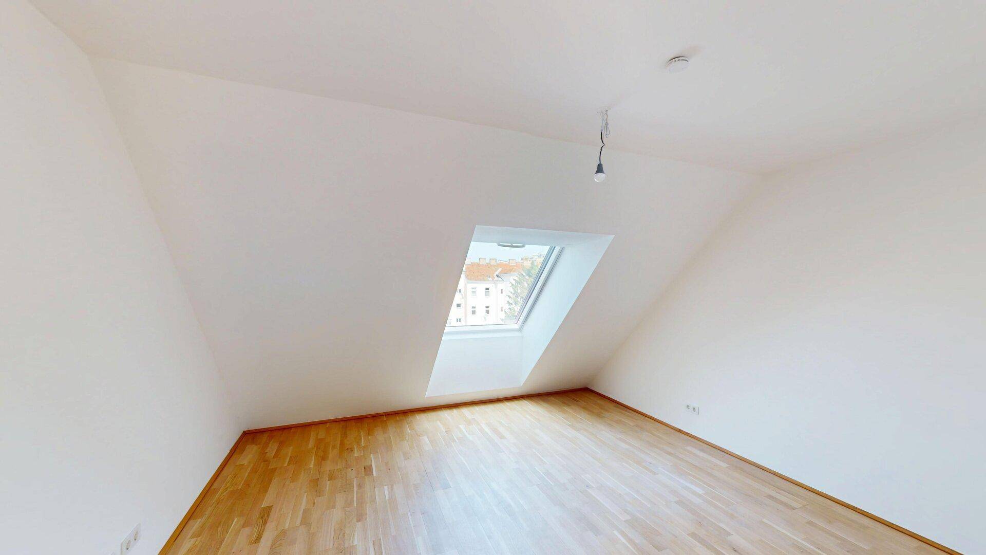 Helles Schlafzimmer im Dachgeschoss mit Holzboden und einem großen Dachfenster.
