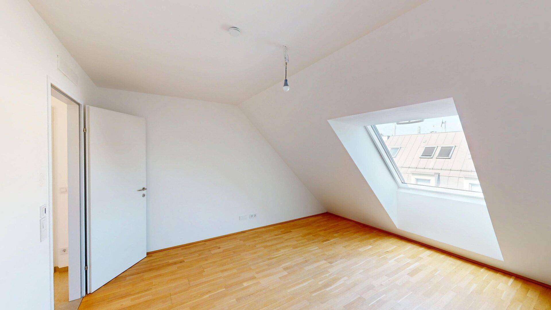 Dachgeschosszimmer mit Holzboden und schrägem Dachfenster, bietet viel Tageslicht.