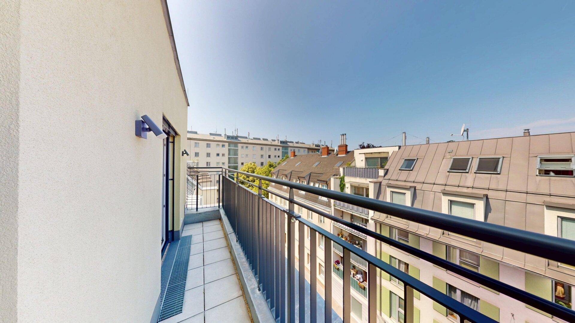 Langer Balkon mit Metallgeländer und Blick auf die umliegenden Gebäude der Stadt.