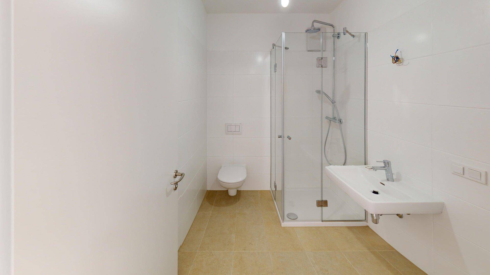 Helles Badezimmer mit Duschkabine, Waschbecken und WC, ausgestattet mit weißen Fliesen.