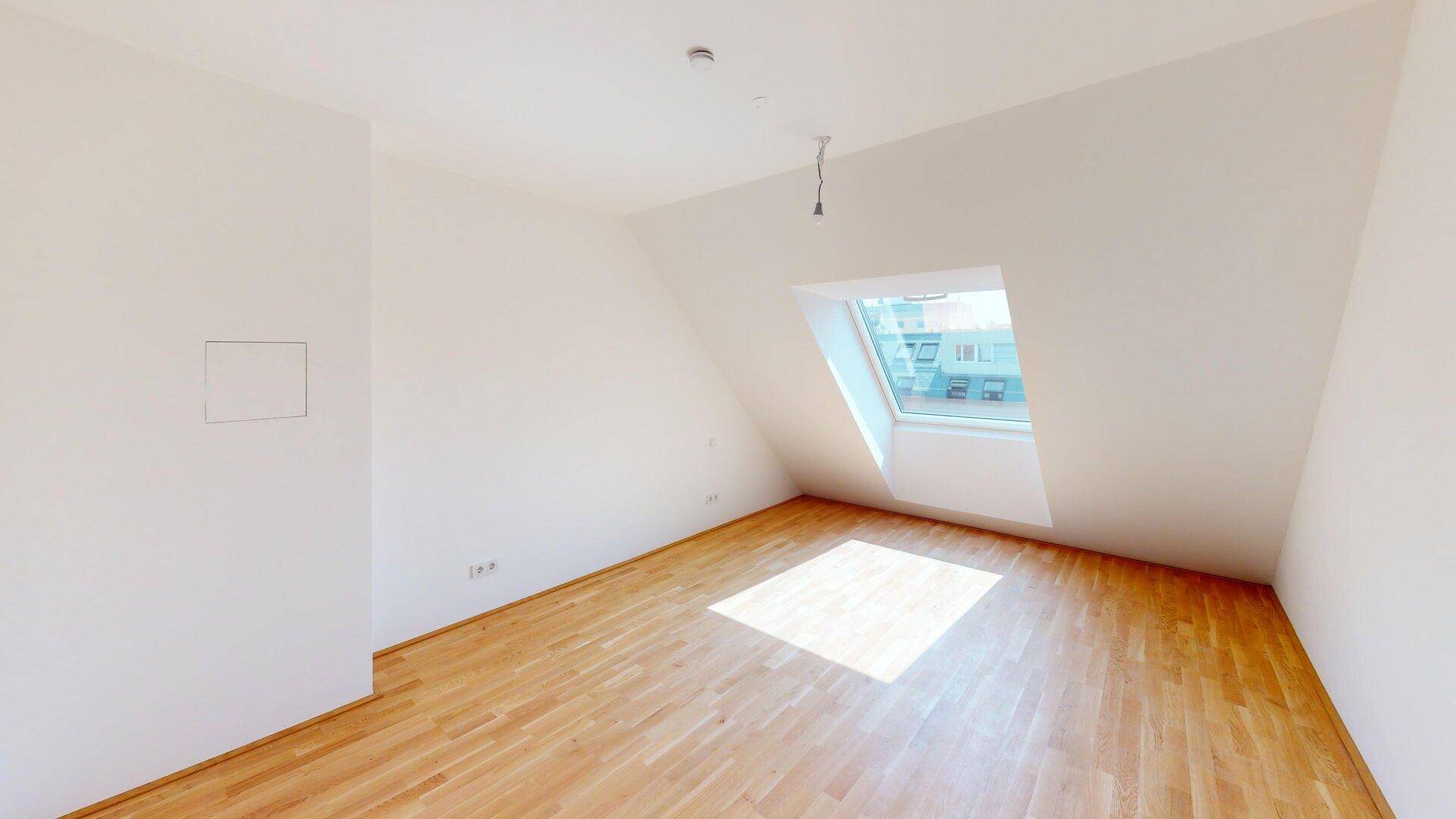 Geräumiges Dachgeschosszimmer mit Holzboden und schrägem Dachfenster, ideal als Schlafzimmer.