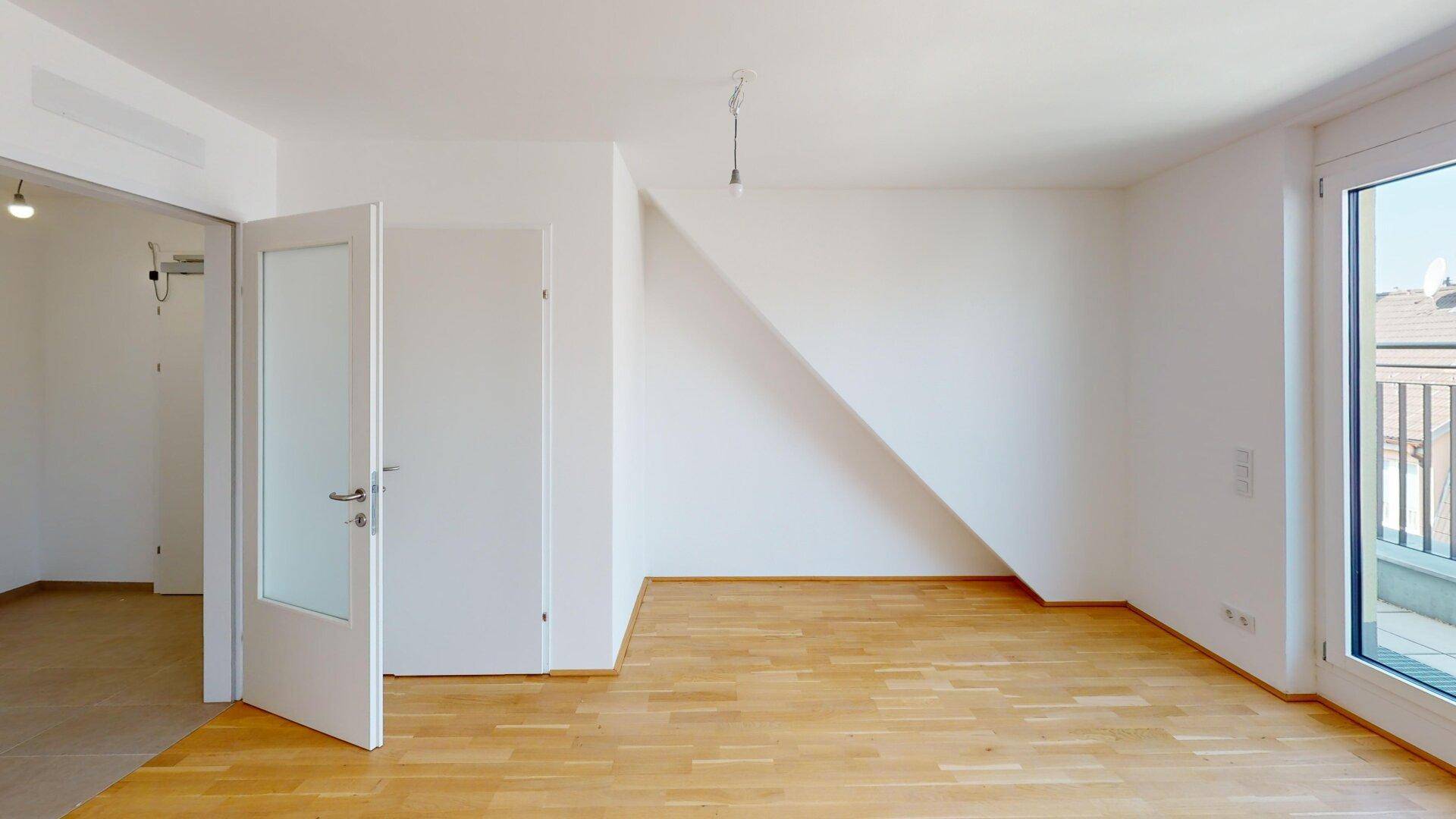 Helles Zimmer mit Parkettboden und Zugang zu einem Balkon, ideal für Wohnzwecke.