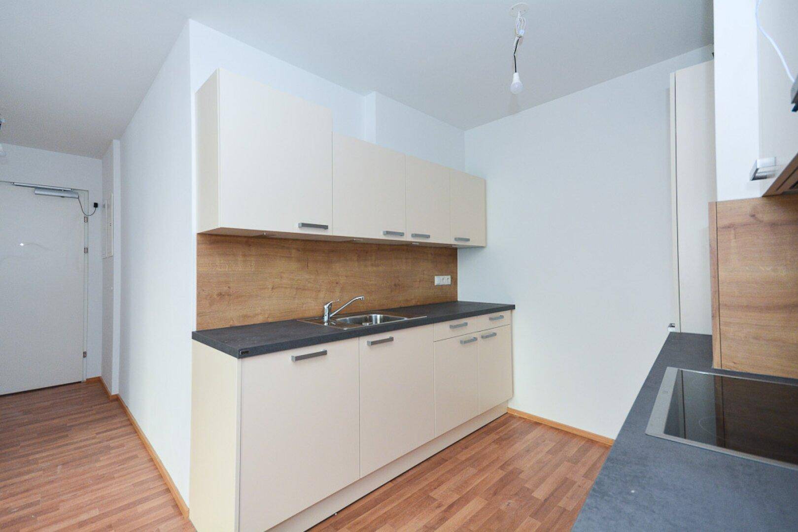 Funktionale Einbauküche mit hellen Schränken, dunkler Arbeitsplatte und Laminatboden.