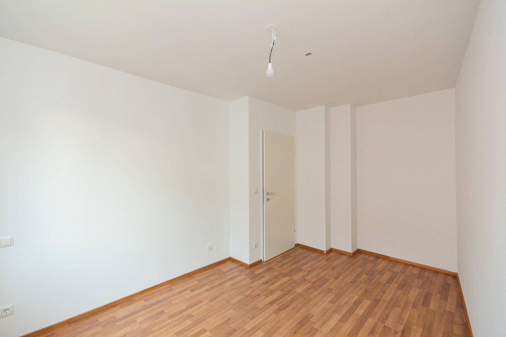 Heller, leerer Raum mit Laminatboden und weißen Wänden, bereit zur individuellen Gestaltung.