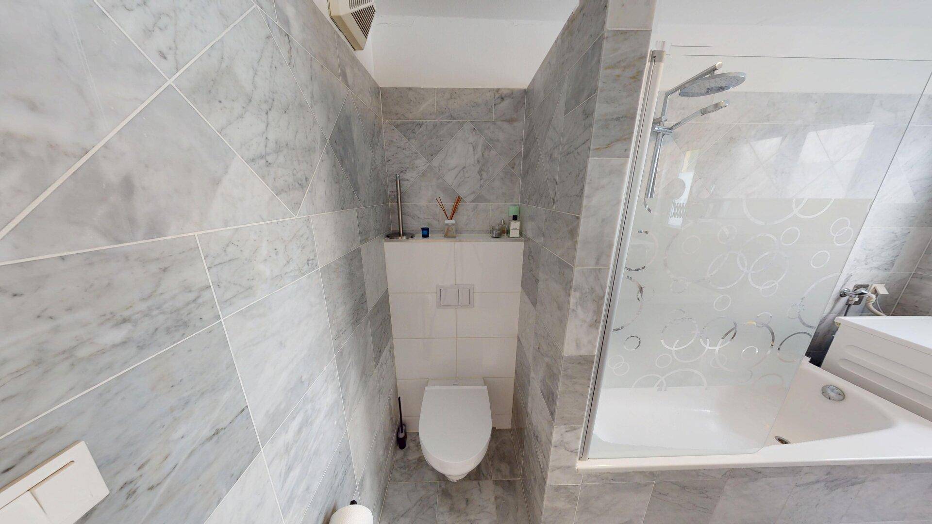 Helles Badezimmer mit Marmorfliesen, Badewanne und integrierter Dusche.