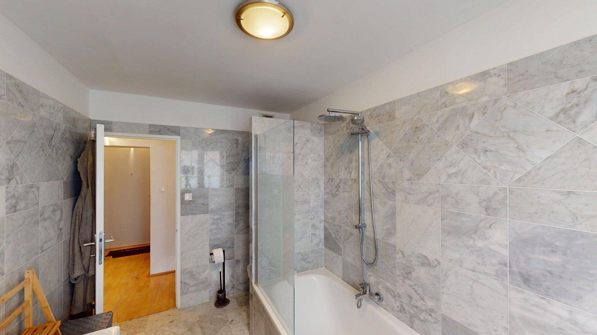 Modernes Badezimmer mit Marmorfliesen, Badewanne und Duschvorrichtung.